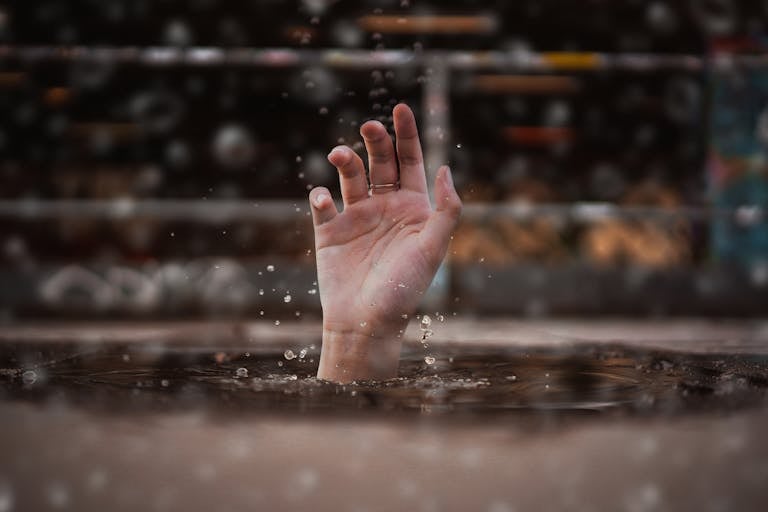 A single hand emerges from water, symbolizing a cry for help amidst a rainy setting.