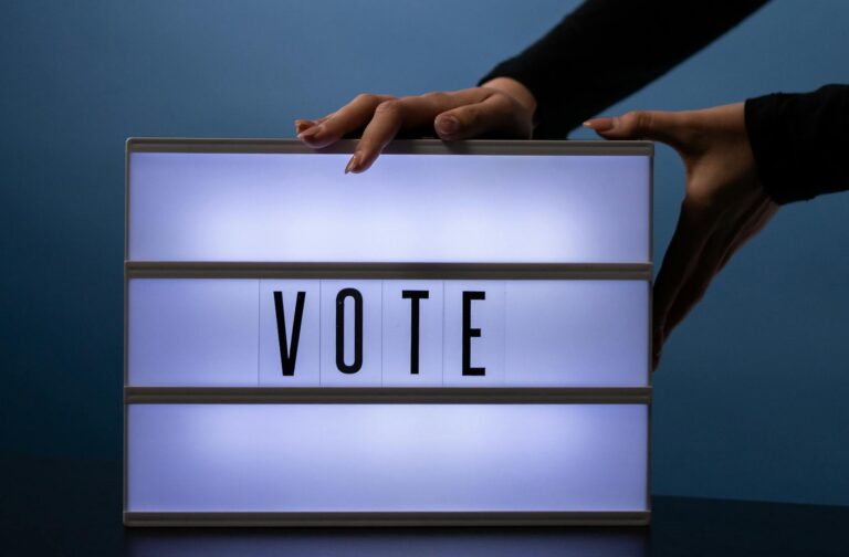 Close-up of hands placing a lit vote sign with a bold message on a blue background.
